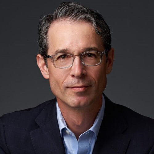 Headshot of David Musto, a man with gray hair and glasses, wearing a dark blazer against a dark background.