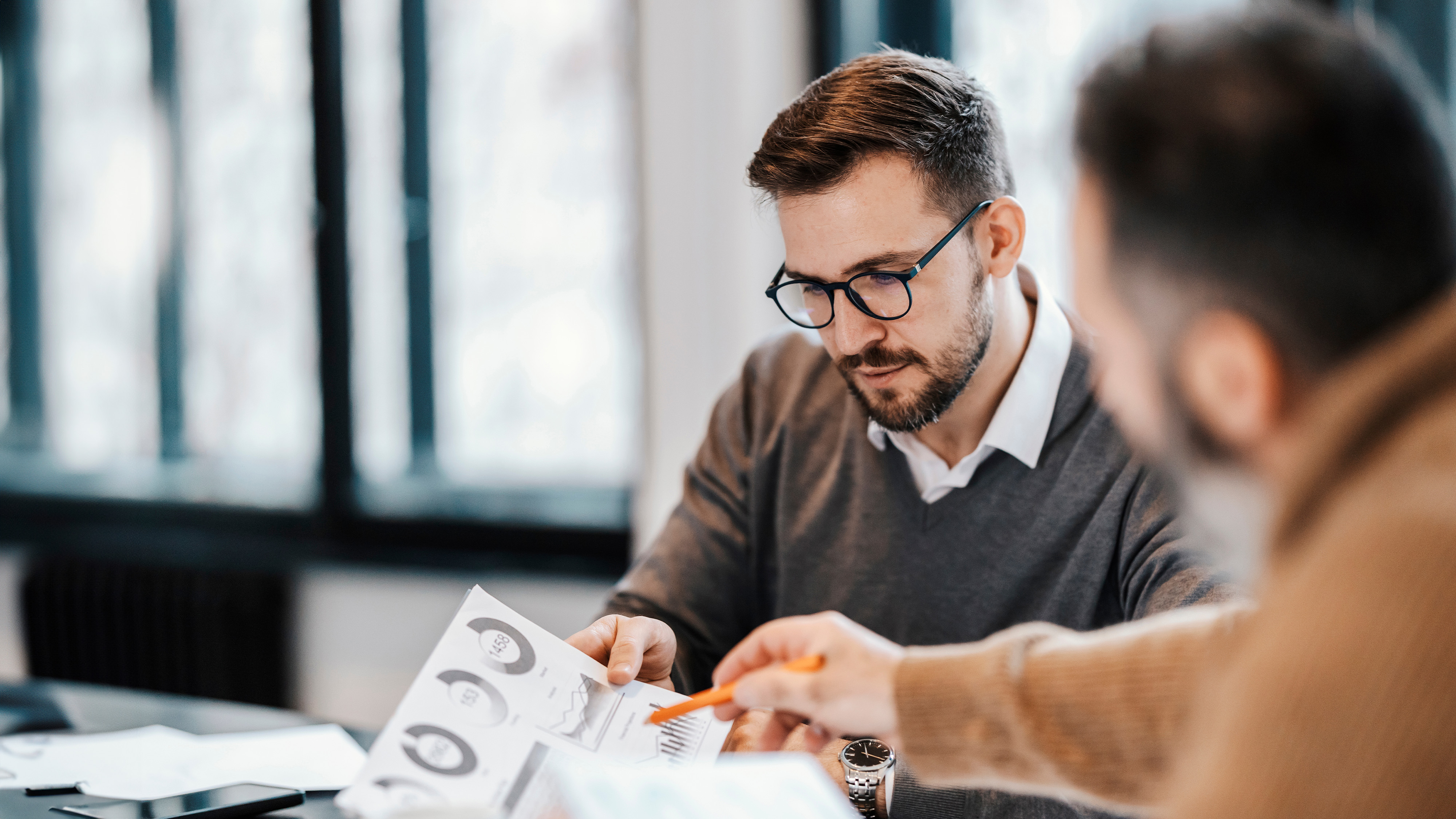 Businessman reviewing a printed report with pie charts and graphs alongside a colleague pointing at the data