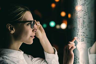 A woman wearing glasses closely examining a lit-up data display at night