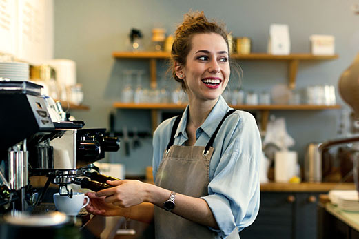 A smiling barista preparing an espresso drink at a coffee shop counter