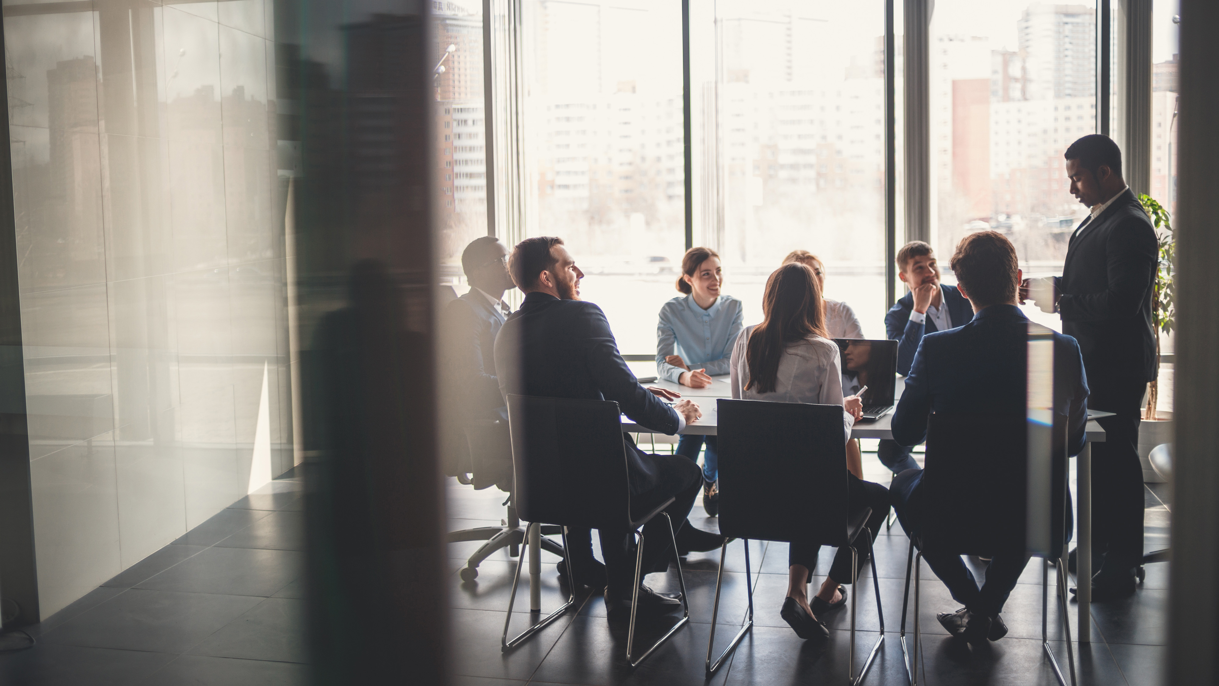 Group of colleagues meeting around a conference table in a glass-walled office