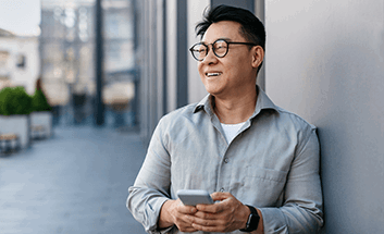 A man smiling and holding his phone while standing outside near a building