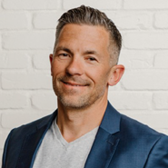 Headshot of a smiling man against a white brick background