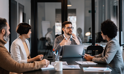Four colleagues discussing business around a conference table with a laptop.