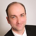 Headshot portrait of Aaron McIsaac in a suit and tie