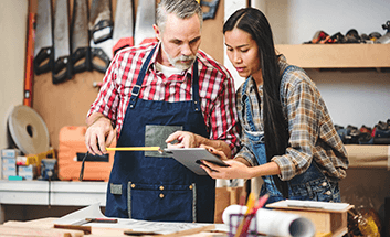 A man and woman in a workshop reviewing plans together on a tablet.