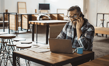 A man talking on the phone while working on a laptop in a co-working space.