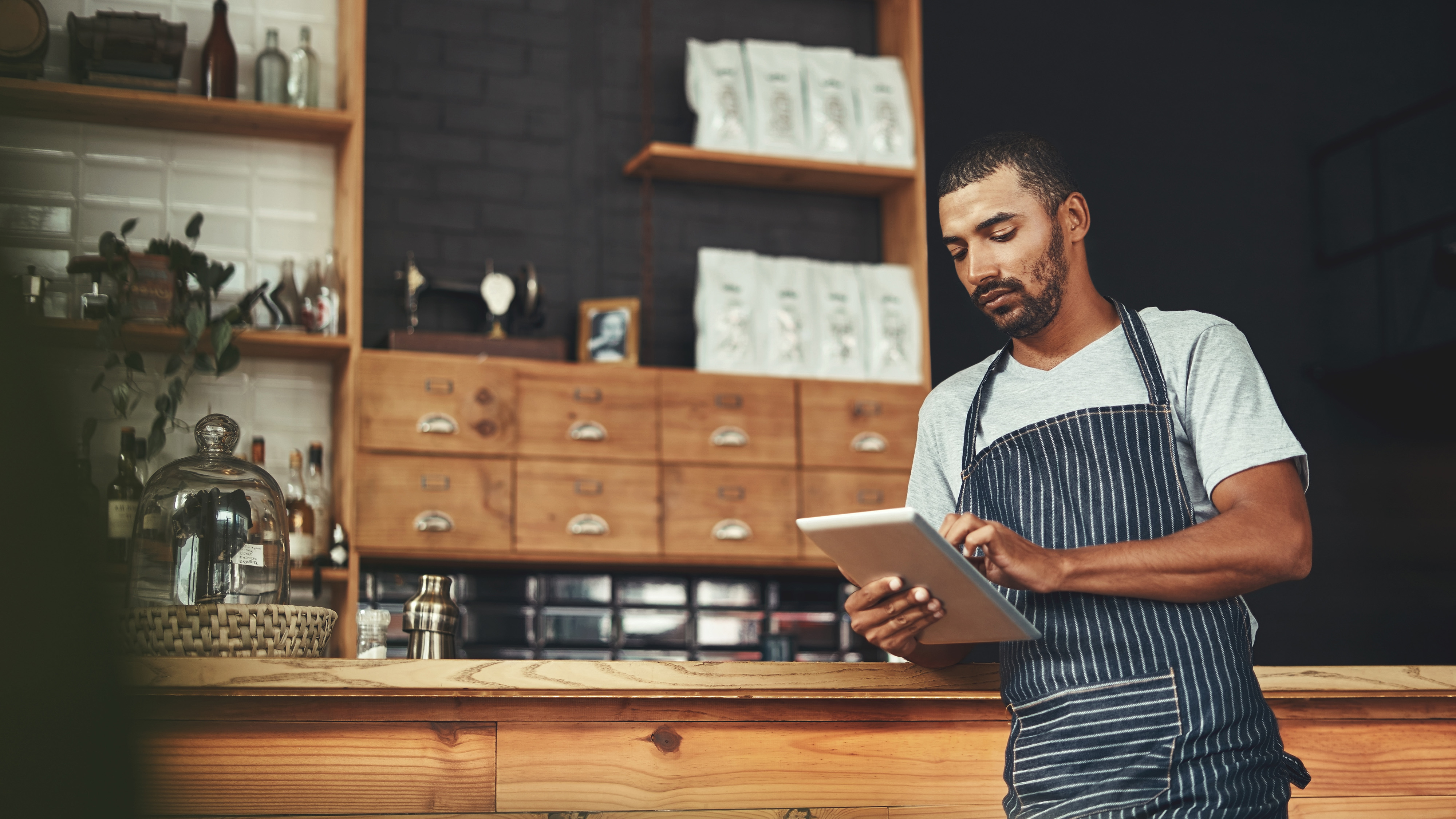 Small business owner in an apron reviewing information on a tablet at a shop counter