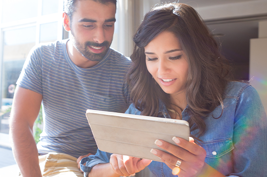 A couple smiling while looking together at a tablet.