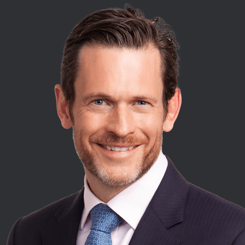 Headshot of Nick Good, a man with a short beard, smiling in a dark suit and white shirt with a patterned tie.