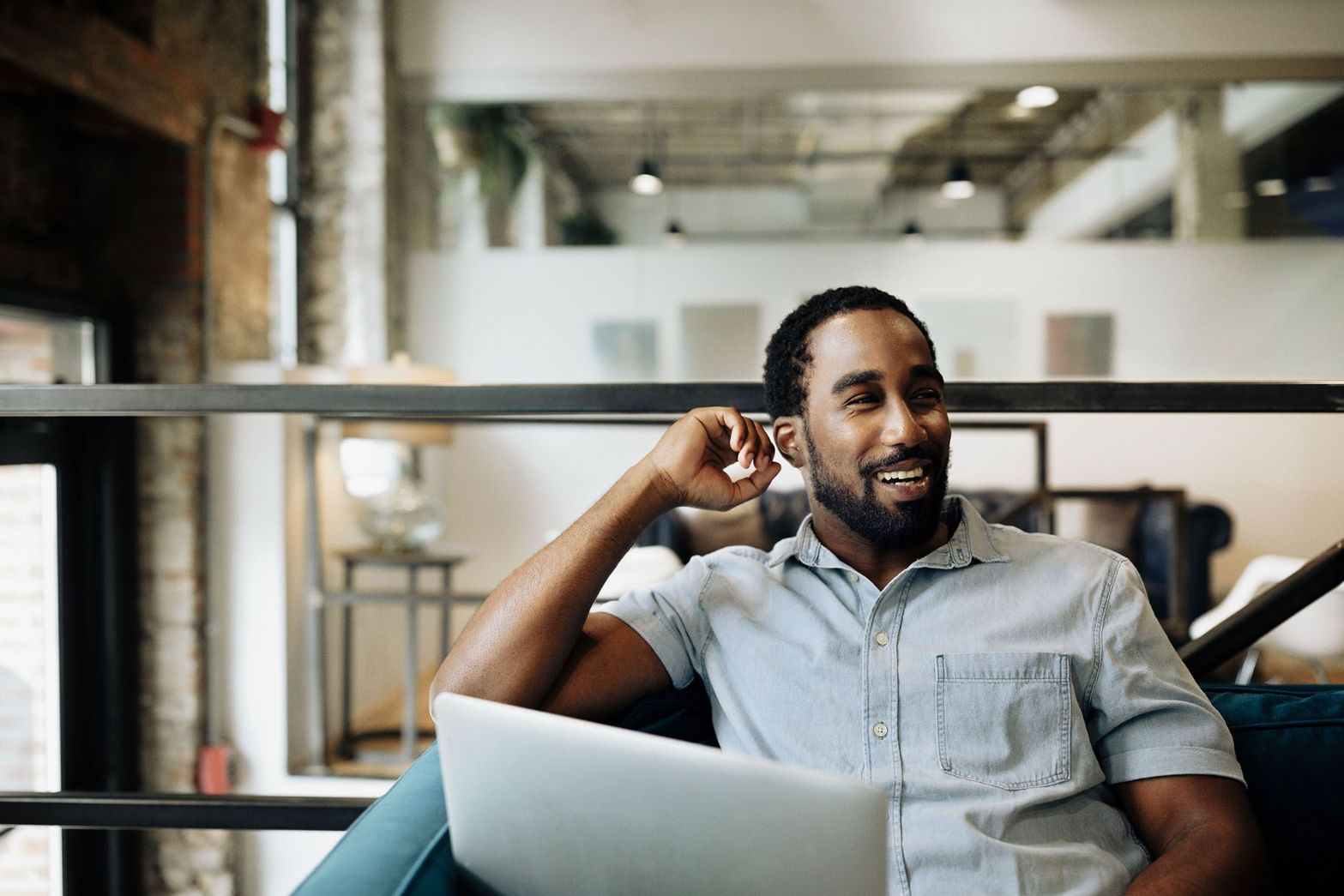 A man smiling and laughing while working on a laptop in a loft-style office