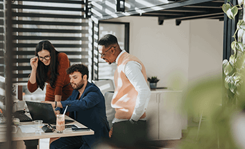 Three coworkers gathered around a laptop in an office