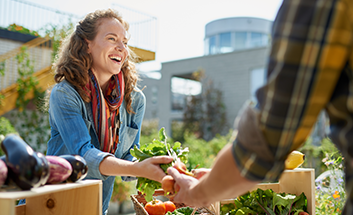 A woman smiling while buying fresh vegetables at an outdoor market stall