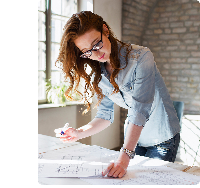 Woman reviewing blueprints on a drafting table by a window