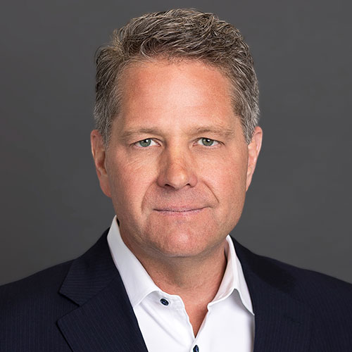 Headshot of Dan Morrison, a man with gray-streaked hair, smiling in a dark suit and white shirt.